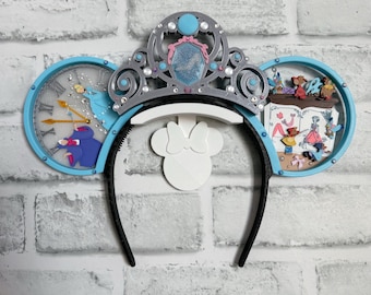 Könnte beinhalten: Ein Paar blaue und silberne Minnie Mouse Ohren mit einem Kronen-Stirnband, einem Zifferblatt auf dem einen Ohr und einer Szene aus dem Film auf dem anderen Ohr.