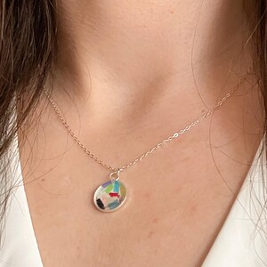 May include: A silver chain necklace with a round pendant featuring a colorful abstract design.
