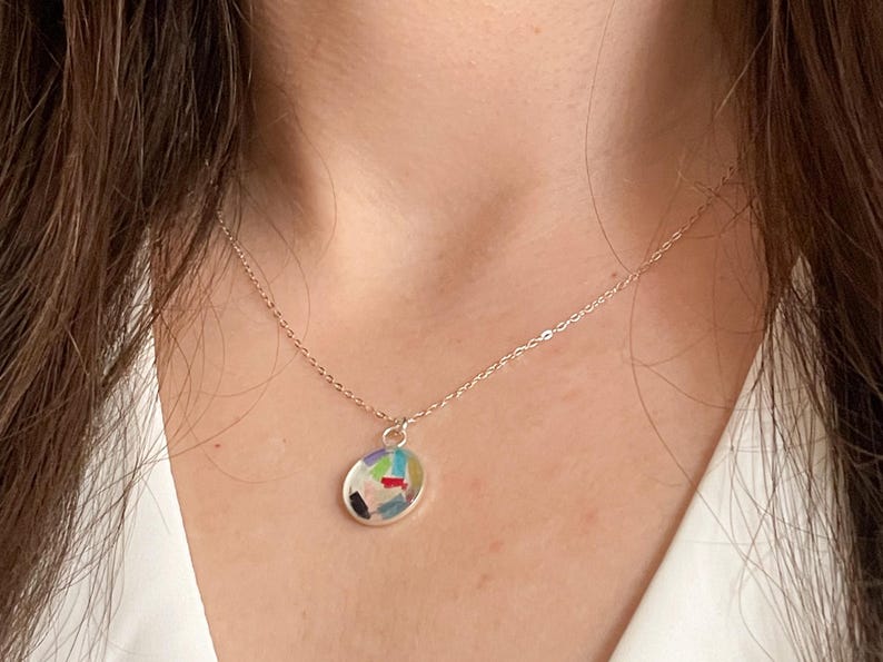 May include: A silver chain necklace with a round pendant featuring a colorful abstract design.