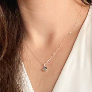 May include: A delicate gold chain necklace with a small round pendant. The pendant has a multi-colored stone or glass design.