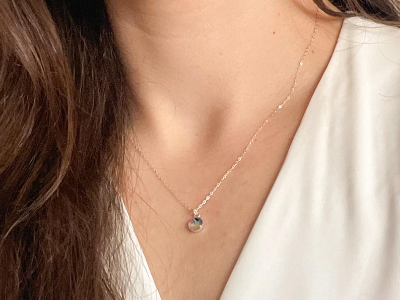 May include: A delicate gold chain necklace with a small round pendant. The pendant has a multi-colored stone or glass design.