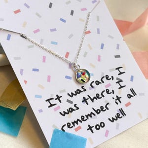 May include: A silver necklace with a small round pendant featuring a colorful abstract design. The necklace comes with a card that reads "It was rare, I was there, I remember it all too well."