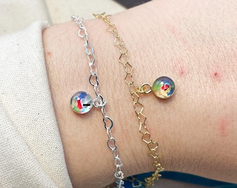May include: Two gold chain bracelets with colorful glass charms. One bracelet has a heart-shaped chain and the other has a round chain.