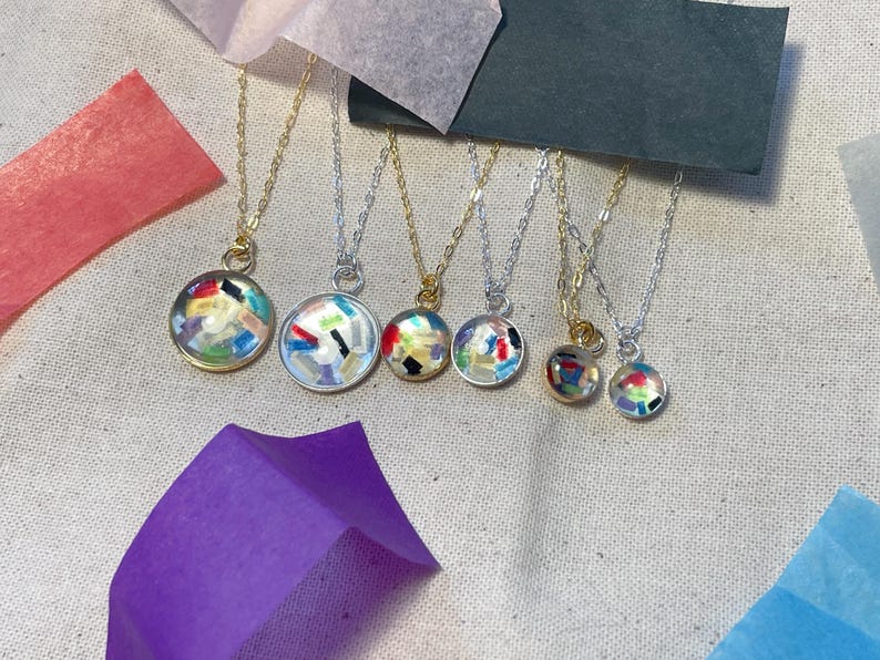 May include: Six necklaces with different colored resin pendants. The pendants are round and filled with colorful confetti-like pieces. The necklaces are on a white background.