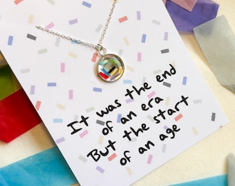 May include: A silver necklace with a round pendant featuring colorful confetti inside. The necklace comes with a card that reads "It was the end of an era but the start of an age."