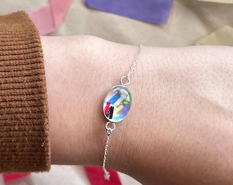 May include: A silver chain bracelet with a clear oval charm filled with colorful confetti-like pieces.
