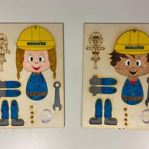 Könnte beinhalten: Zwei Holzpuzzles mit Comicfiguren in Bauarbeiterkleidung. Jedes Puzzle zeigt einen gelben Helm mit dem Wort "KOMATSU", blaue Overalls und separate Teile für Arme, Beine und Werkzeuge. Die Puzzles befinden sich auf einem hellen Hintergrund.