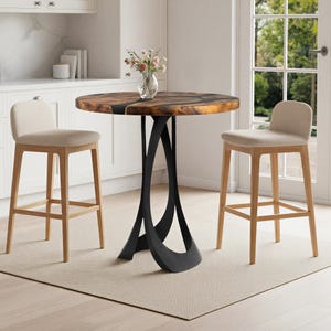 May include: A round wooden table with a dark, intricate design and a black metal base. Two beige upholstered bar stools flank the table. A vase of flowers sits on the table. The table is approximately 91 cm in diameter.