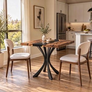 May include: A square dining table with a natural wood grain top featuring a black resin inlay, supported by a curved black metal base, accompanied by two chairs with dark wood frames and light beige upholstered seats.