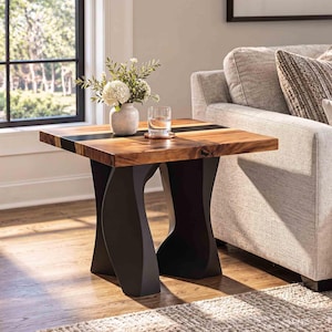 May include: A square side table featuring a natural wood grain top with a dark resin inlay, supported by two curved matte black legs. A light-colored ceramic vase with white flowers and a clear glass tumbler sit on the table surface.