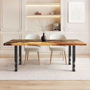 May include: A rectangular wooden dining table with a dark epoxy resin inlay. The table has black metal legs and is surrounded by two upholstered chairs. A vase with branches sits on the table. The table measures approximately 183 cm long.