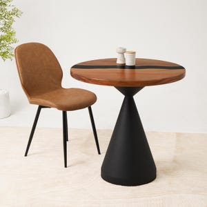 May include: A round wooden table with a black resin inlay and a black conical pedestal base, accompanied by a tan faux leather chair with black metal legs. Two small white decorative objects sit on the table surface.