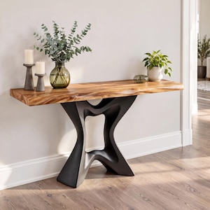 May include: A console table featuring a natural live-edge wood top with a rich brown grain and a sculptural matte black base. On the surface are two gray pillar candle holders, a green glass vase with eucalyptus, and a small potted plant.