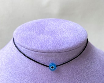 Pode incluir: Um colar choker preto com um pequeno amuleto azul de olho turco.