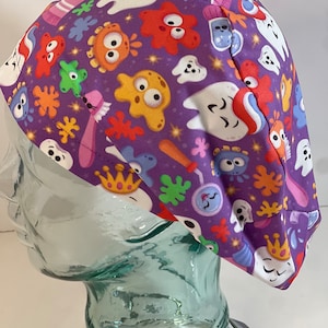May include: Purple scrub hat with a colorful pattern of teeth, toothbrushes, and cartoon characters. The hat has a white elastic band.