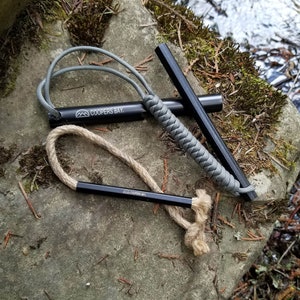 May include: A black fire starter with a gray paracord handle and a tan rope. The fire starter is labeled "Coopers Bay".