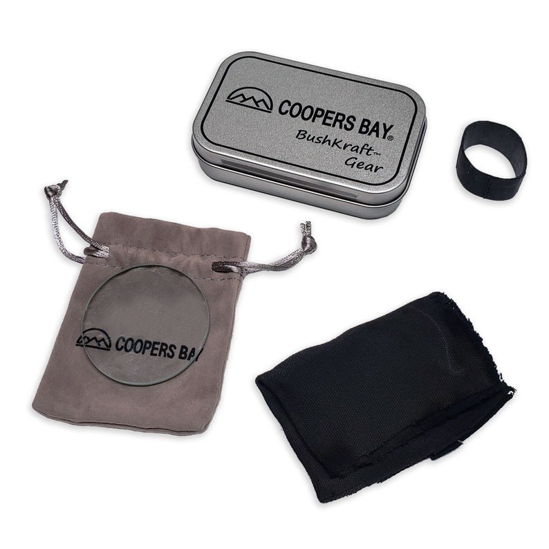 Puede incluir: Una lata plateada con el texto "Coopers Bay Bushkraft Gear" en ella. La lata est&aacute; al lado de una bolsa gris con una lente redonda de vidrio en su interior. La bolsa tiene el texto "Coopers Bay" en ella. Tambi&eacute;n hay una bolsa negra y una banda el&aacute;stica negra.