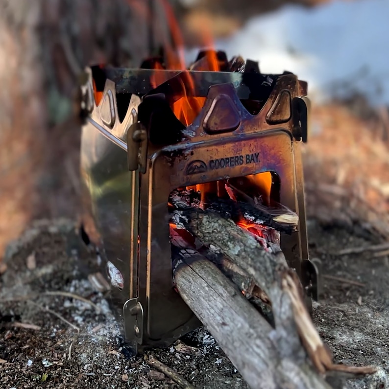 Peut inclure: Un po&ecirc;le &agrave; bois portable de petite taille avec un feu qui br&ucirc;le &agrave; l'int&eacute;rieur. Le po&ecirc;le est en m&eacute;tal et a une finition noire. Le po&ecirc;le est marqu&eacute; "Coopers Bay".