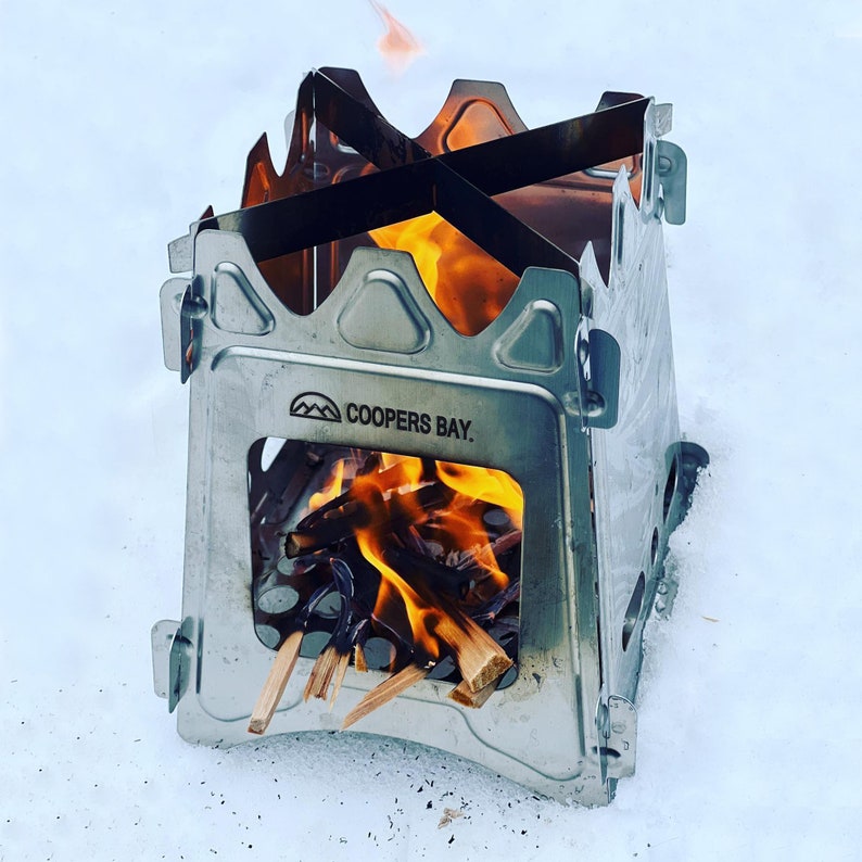 Peut inclure: Un r&eacute;chaud de camping en m&eacute;tal argent&eacute; avec un feu qui br&ucirc;le &agrave; l'int&eacute;rieur. Le r&eacute;chaud porte un logo qui dit "Coopers Bay."