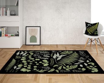 May include: A black and green area rug with a botanical pattern featuring various leaves and ferns. The rug is laid out on a wood floor in a living room setting.