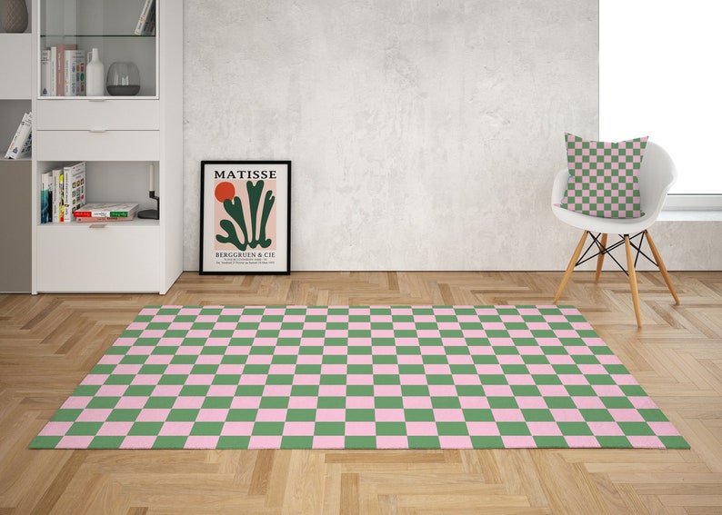 Puede incluir: Una alfombra a cuadros verde y rosa con una silla blanca y una almohada con un patr&oacute;n a cuadros verde y rosa en el fondo. La alfombra est&aacute; sobre un suelo de madera.