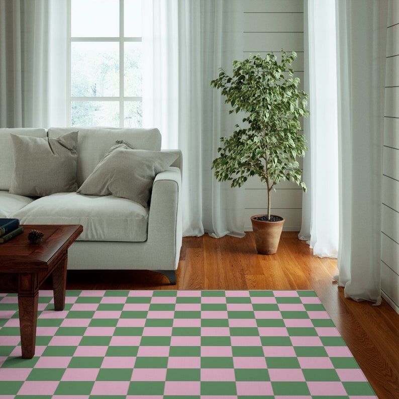 Puede incluir: Una alfombra de &aacute;rea a cuadros verde y rosa en un ambiente de sala de estar. La alfombra est&aacute; frente a un sof&aacute; blanco con almohadas y una mesa de caf&eacute; de madera. Una planta en maceta est&aacute; en la esquina de la habitaci&oacute;n.