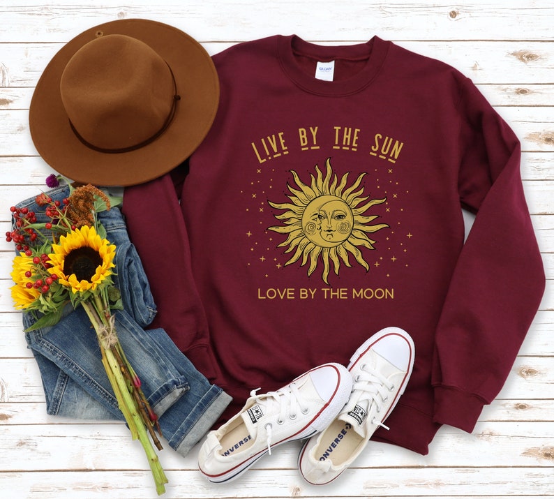 May include: Burgundy sweatshirt with a gold sun and moon graphic and the text "Live by the sun, love by the moon".