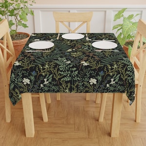 May include: A black tablecloth with a floral pattern featuring green leaves and white flowers. The tablecloth is laid on a wooden table with four chairs and white plates.