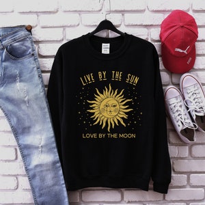 May include: Black sweatshirt featuring a gold sun and moon graphic with the text "Live by the sun, love by the moon".