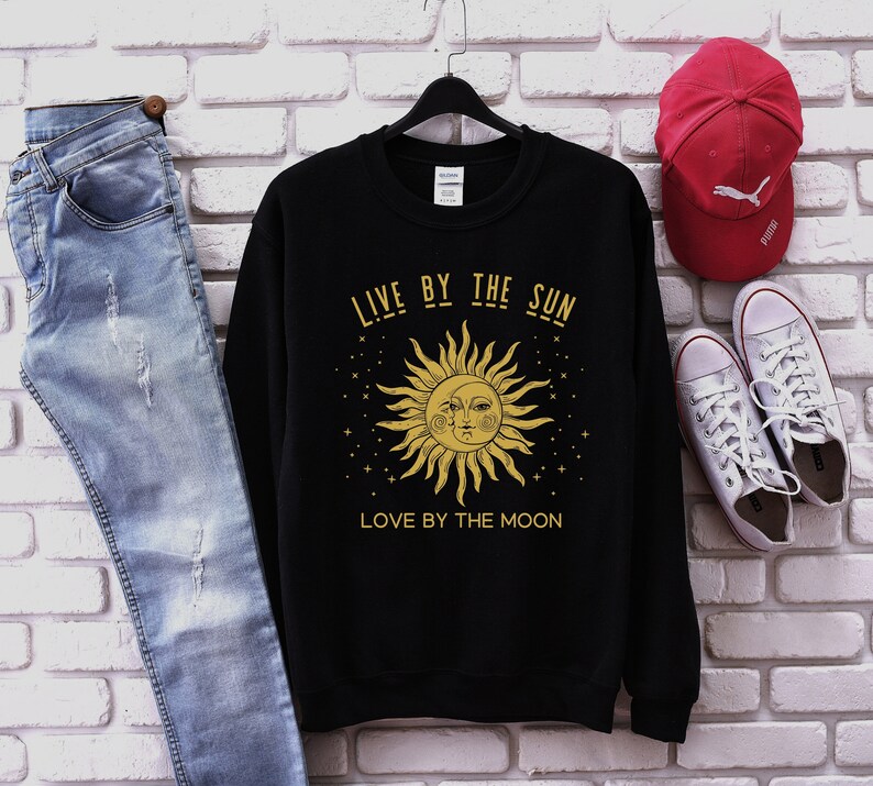 May include: Black sweatshirt featuring a gold sun and moon graphic with the text "Live by the sun, love by the moon".