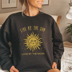 May include: Black sweatshirt with a gold sun and moon graphic and the text "Live by the sun, love by the moon".