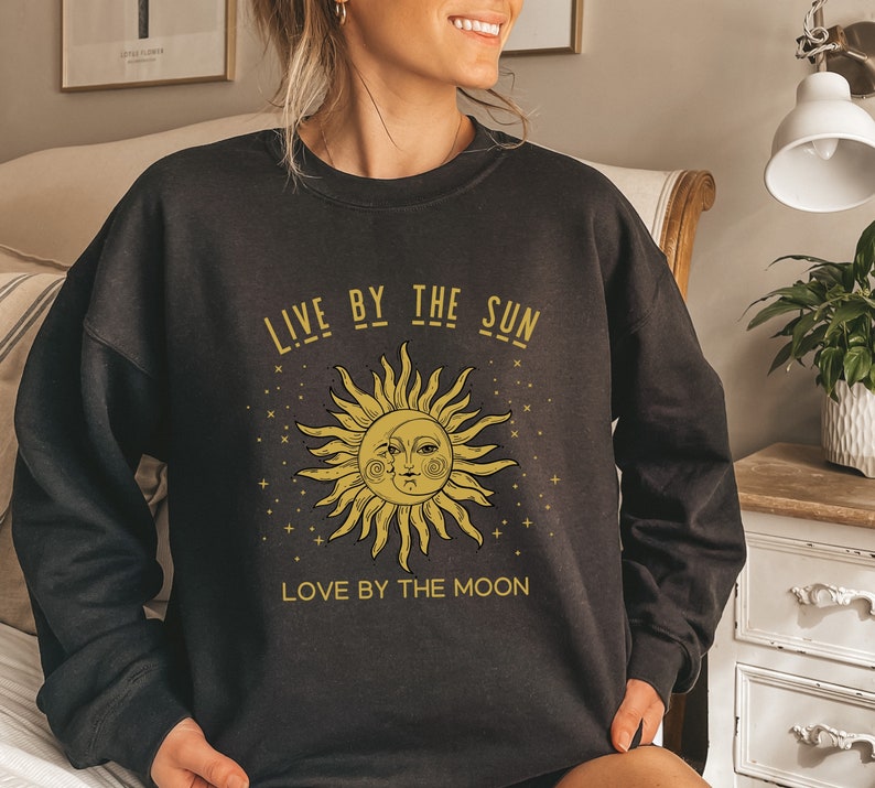 May include: Black sweatshirt with a gold sun and moon graphic and the text "Live by the sun, love by the moon".
