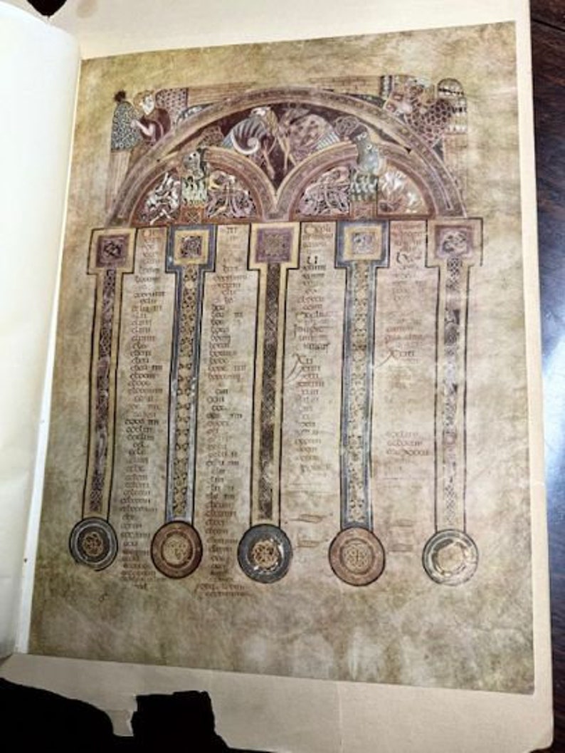 May include: A close-up of a page from an old book with a detailed illustration of a medieval manuscript. The illustration is in shades of brown, black, and white and features a series of columns with text and decorative elements. The text is in a medieval script.