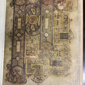 May include: A close-up of a page from an illuminated manuscript, featuring intricate gold and black designs with a small figure in the top right corner.