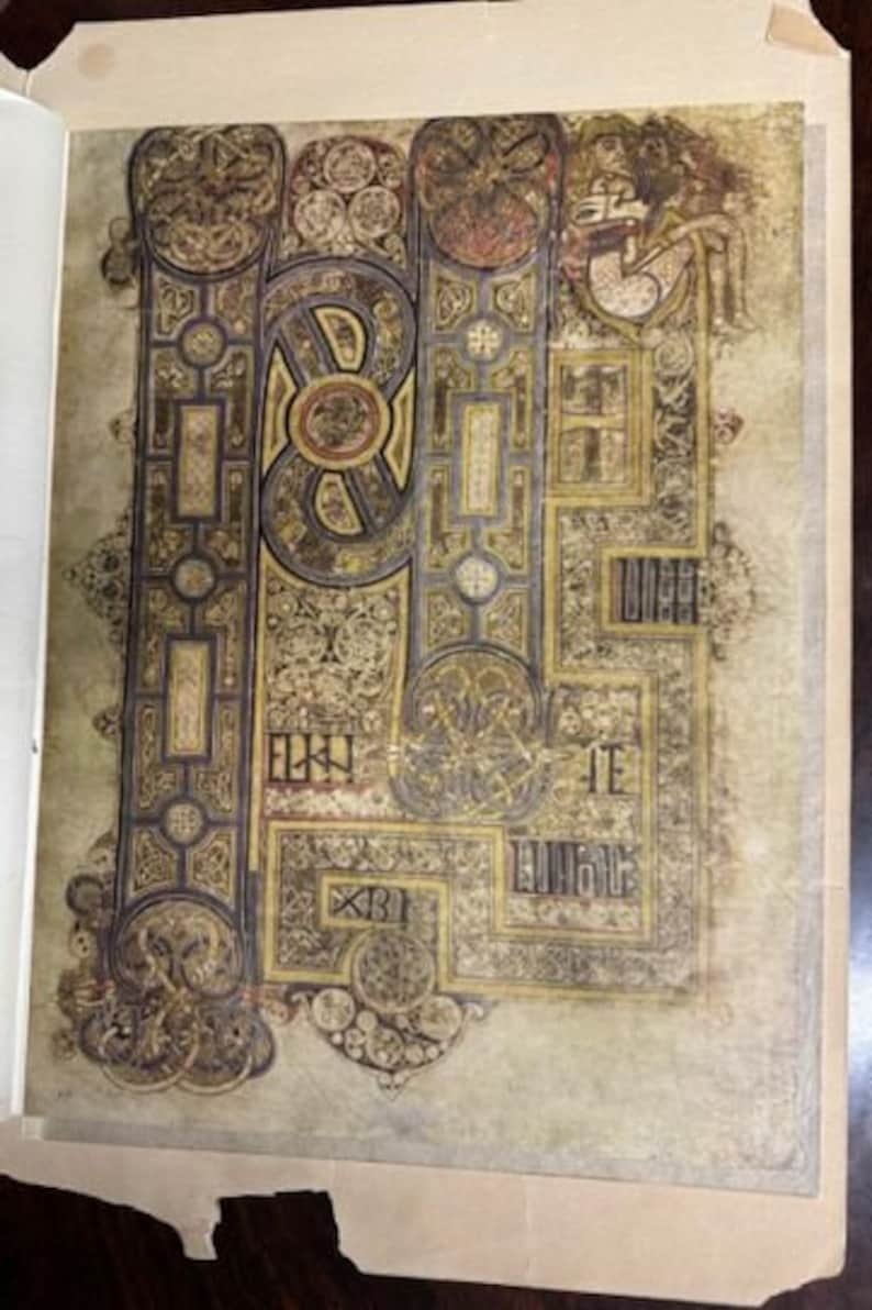 May include: A close-up of a page from an illuminated manuscript, featuring intricate gold and black designs with a small figure in the top right corner.