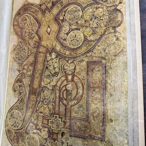 May include: A close-up of a page from the Book of Kells, an illuminated manuscript dating from the 9th century. The page features intricate Celtic knotwork in gold, red, and black, with the word "Incipit" written in a decorative script.