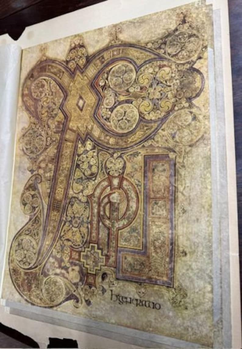 May include: A close-up of a page from the Book of Kells, an illuminated manuscript dating from the 9th century. The page features intricate Celtic knotwork in gold, red, and black, with the word "Incipit" written in a decorative script.