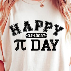 Pu&ograve; includere: T-shirt color crema con le parole "HAPPY" e "&pi; DAY" in grassetto nero, in stile collegiale. La data "3.14.2027" &egrave; centrata tra le parole "HAPPY" e "&pi; DAY". &Egrave; un capo casual per tutti i giorni.