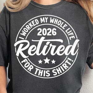 Puede incluir: Camiseta gris oscuro con el texto "I WORKED MY WHOLE LIFE 2026 Retired FOR THIS SHIRT!" en un diseño circular blanco. La camiseta también tiene las palabras "LITTLEGLINTDESIGN" y "digital download" impresas.