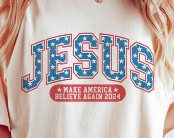 Op de afbeelding: Een wit T-shirt met een blauwe en rode "JESUS"-afbeelding met sterren. De afbeelding bevat ook de tekst "MAKE AMERICA BELIEVE AGAIN 2024".