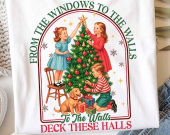 Könnte beinhalten: Weißes T-Shirt mit einem weihnachtlichen Design. Die Grafik zeigt Kinder beim Schmücken eines Baumes, einen Hund, Geschenke und den Text "From the windows to the walls, deck these halls."