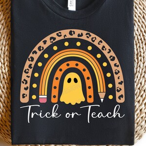 May include: Black t-shirt with a rainbow design featuring a ghost and pencils. The rainbow is outlined with leopard print and has yellow polka dots. The text "Trick or Teach" is below the rainbow.