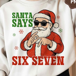 May include: White sweatshirt with a graphic of Santa Claus wearing sunglasses and making a hand gesture. The text "SANTA SAYS SIX SEVEN" is printed in green and red. Festive snowflakes are scattered around the design.