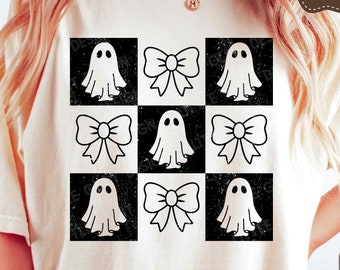 May include: A white t-shirt with a black and white checkered pattern featuring ghosts and bows. The design has a distressed look.