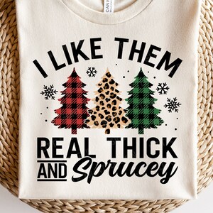 May include: A white t-shirt with the text "I like them real thick and spruce" and a graphic of three Christmas trees. The trees are decorated with red and black plaid, leopard print, and green and black plaid.