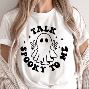 May include: White t-shirt with a black graphic of a ghost with peace signs and the text "Talk Spooky To Me".