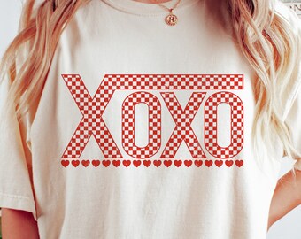 May include: A white t-shirt with a red and white checkered "XOXO" graphic and a row of red hearts below the text.