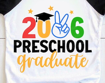 May include: White and black raglan style t-shirt with the text "2026 Preschool Graduate" in red, orange, blue, and green. The design includes a graduation cap and stars. A fun shirt for a preschool graduate.