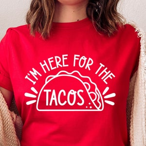 Puede incluir: Camiseta roja con el texto blanco "I'M HERE FOR THE TACOS" y un gr&aacute;fico de taco. La camiseta es de manga corta.