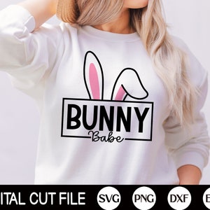 Może przedstawiać: Biała bluza z czarnym obrysem uszu króliczych i tekstem "Bunny Babe" w czarnym prostokącie.